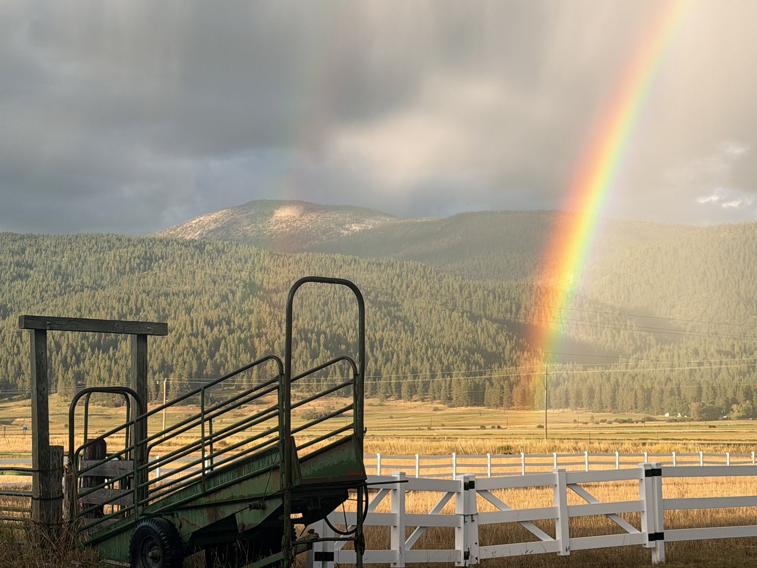 A rainbow over the timbered hills of Meadows Valley, behind the ranch's loading chute and white fence